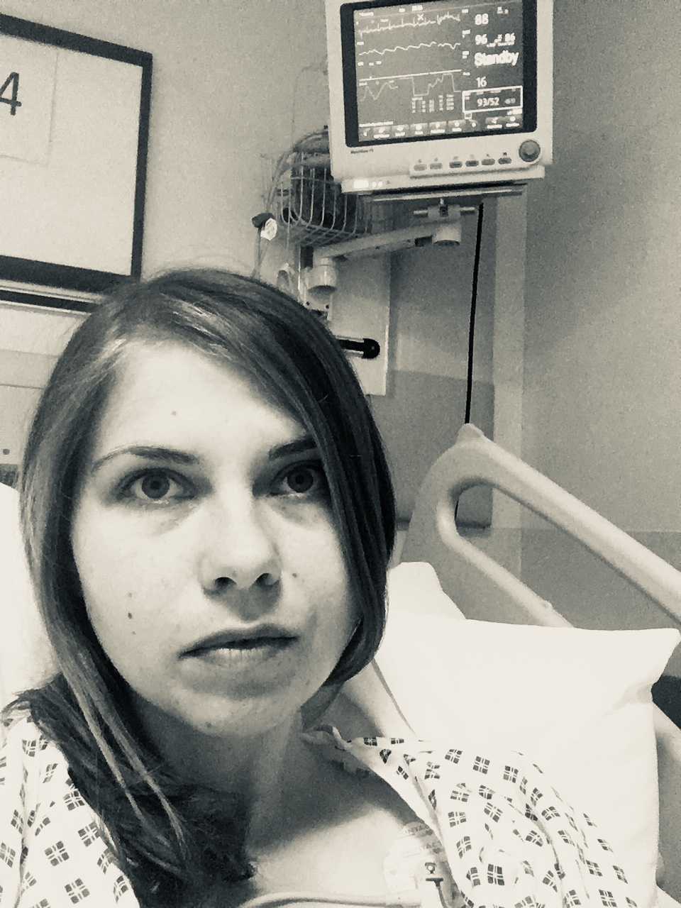 A black and white photo of me with the screen above me again in the hospital bed with the gown on. 