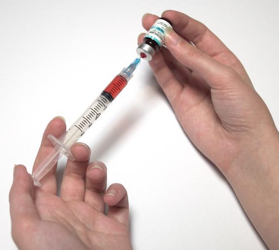 A close up photo of someone loading a syringe from a small bottle.