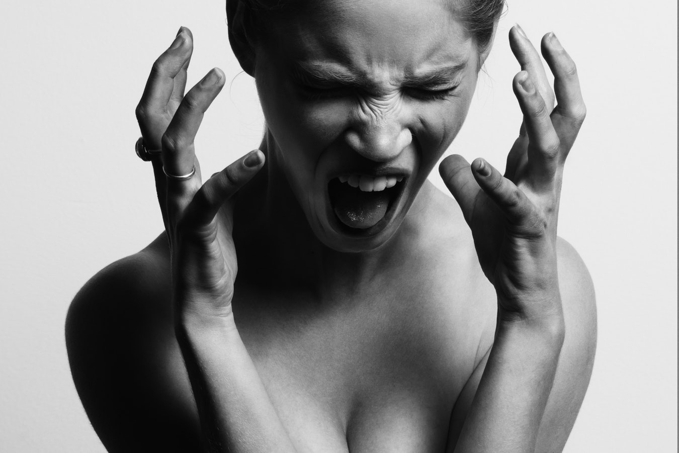 A black and white shot of a woman head down and screaming, hands raised to her face.