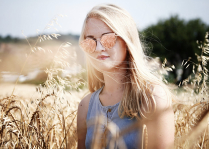 A blonde woman in a field. She's wearing sunglasses and a sleeveless top.