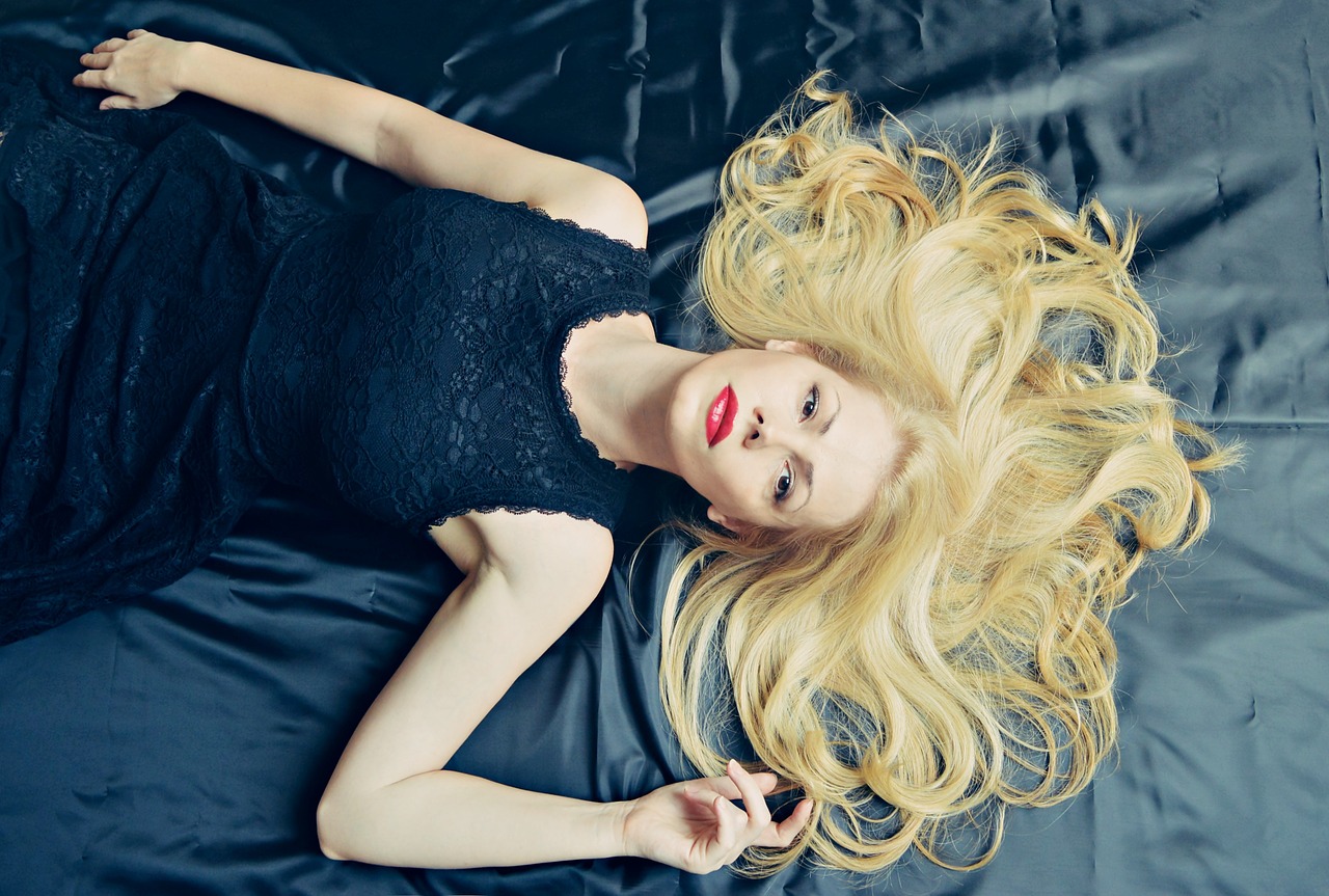 A birds-eye view of a woman lying on a bed, with her blonde hair spread out around her.