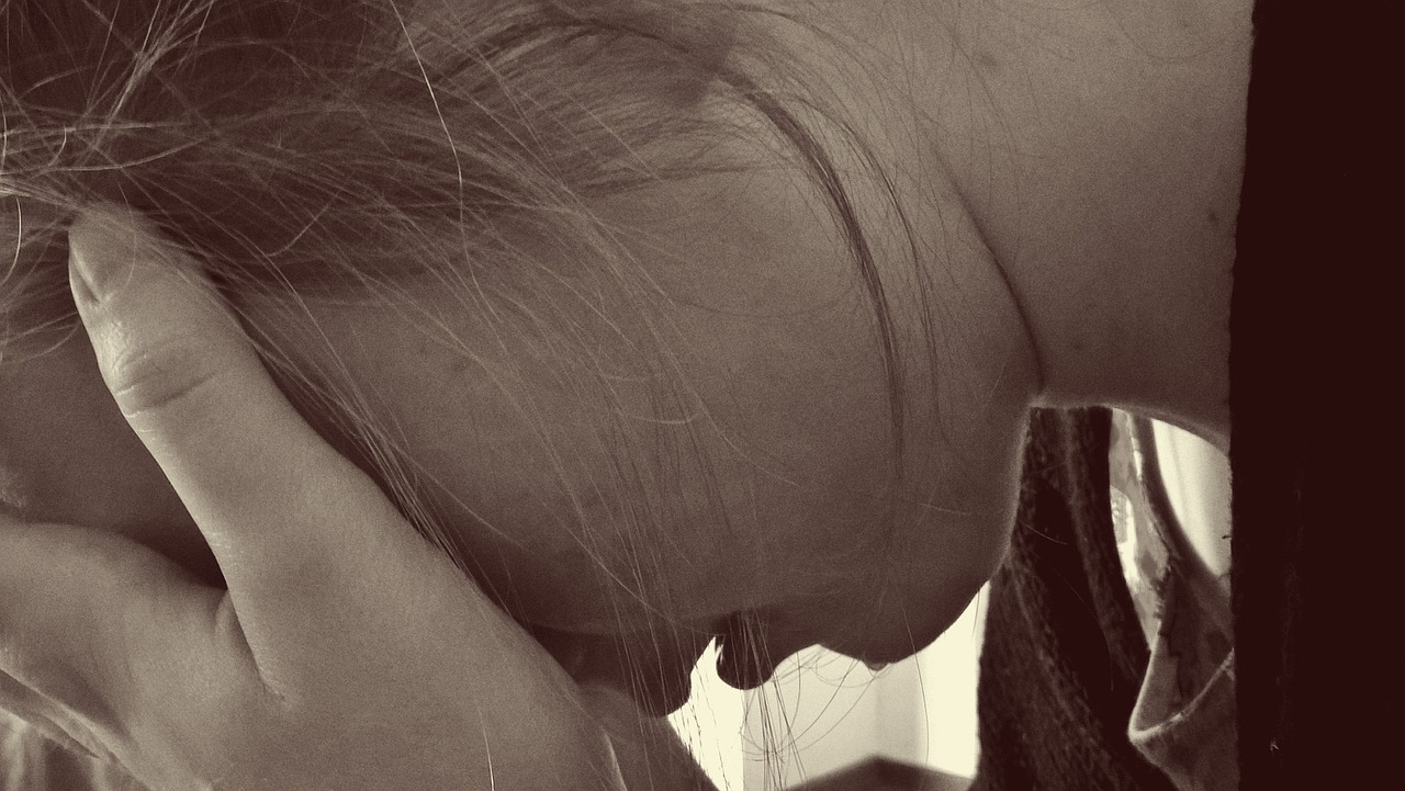 A close-up photo in sepia of a girl in profile. She has her head in her hands and appears to be crying.