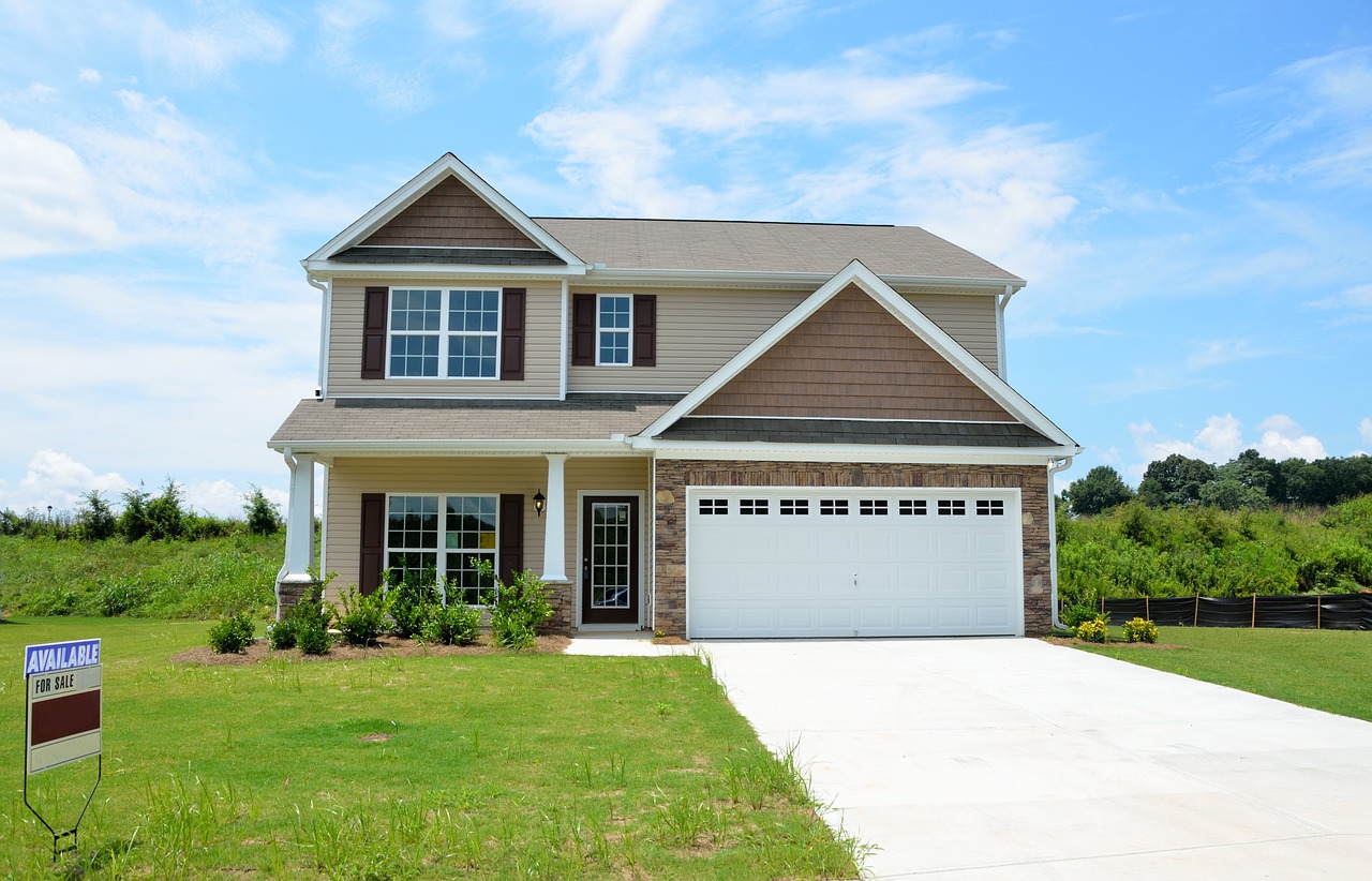 A photo of a house with green grass all around, along with an integral garage and driveway out front. 