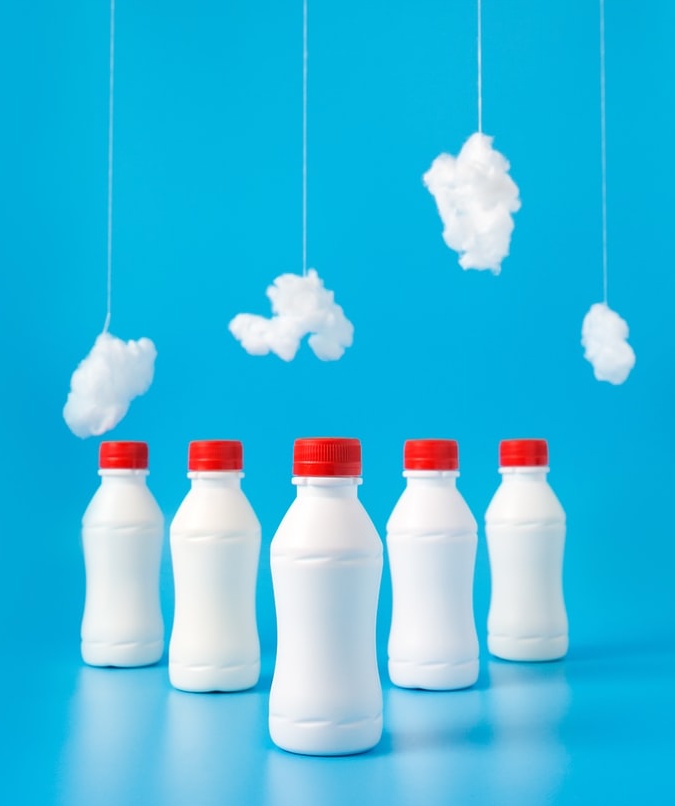 A photo of 5 white milk bottles with red lids against a fully blue background. There are fluffy cotton wool 'clouds' suspended by string hanging above them.