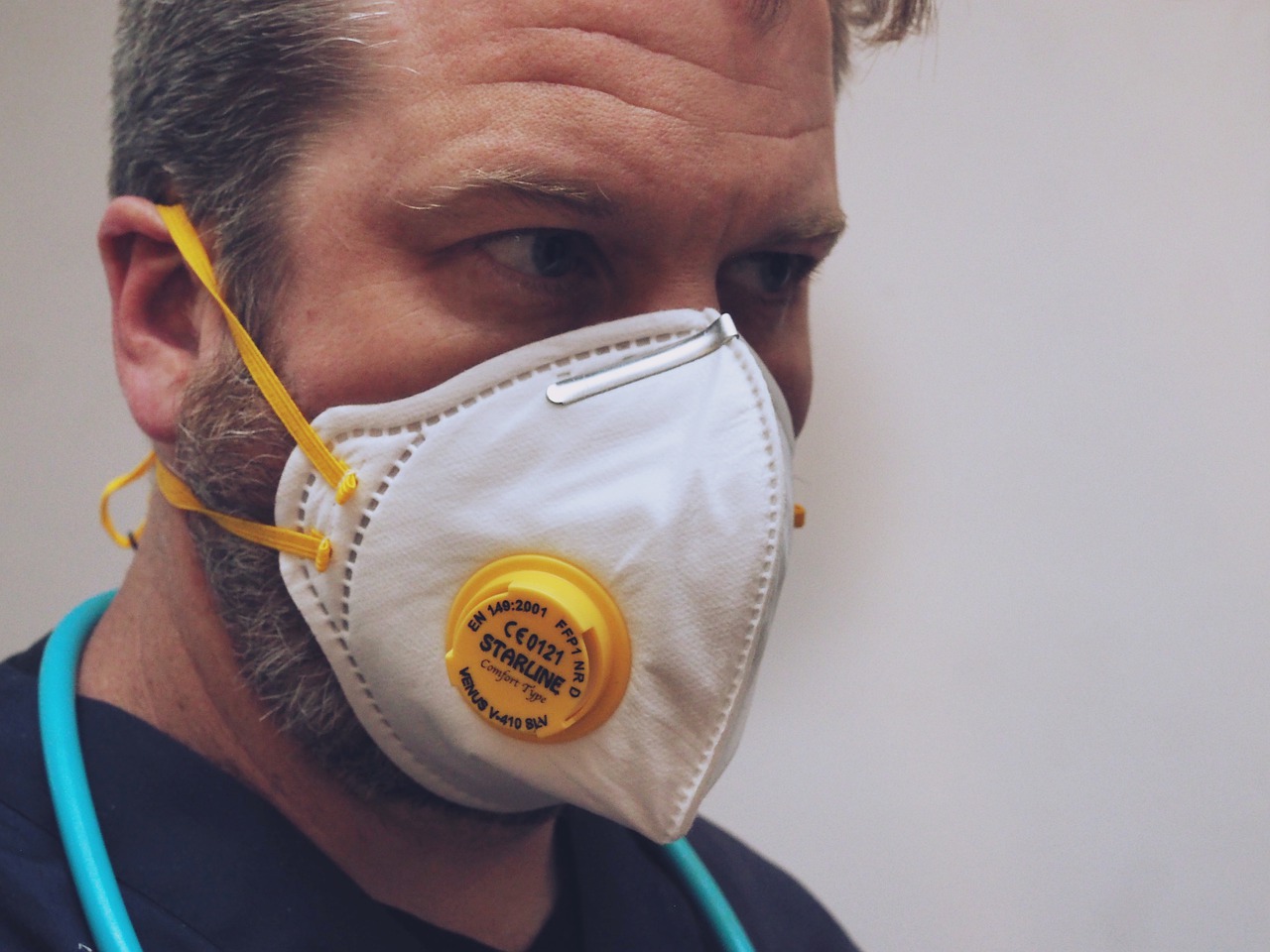 Man wearing valved face mask, with what looks like the top part of a stethoscope around his neck.