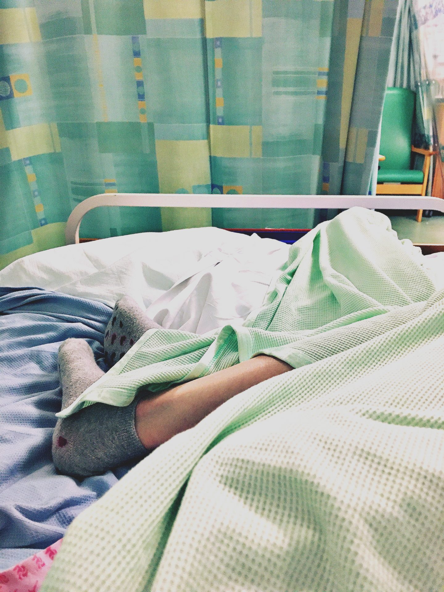 A photo I took looking town at my legs wrapped in green and blue blankets on the bed in the ward after my A&E admission.