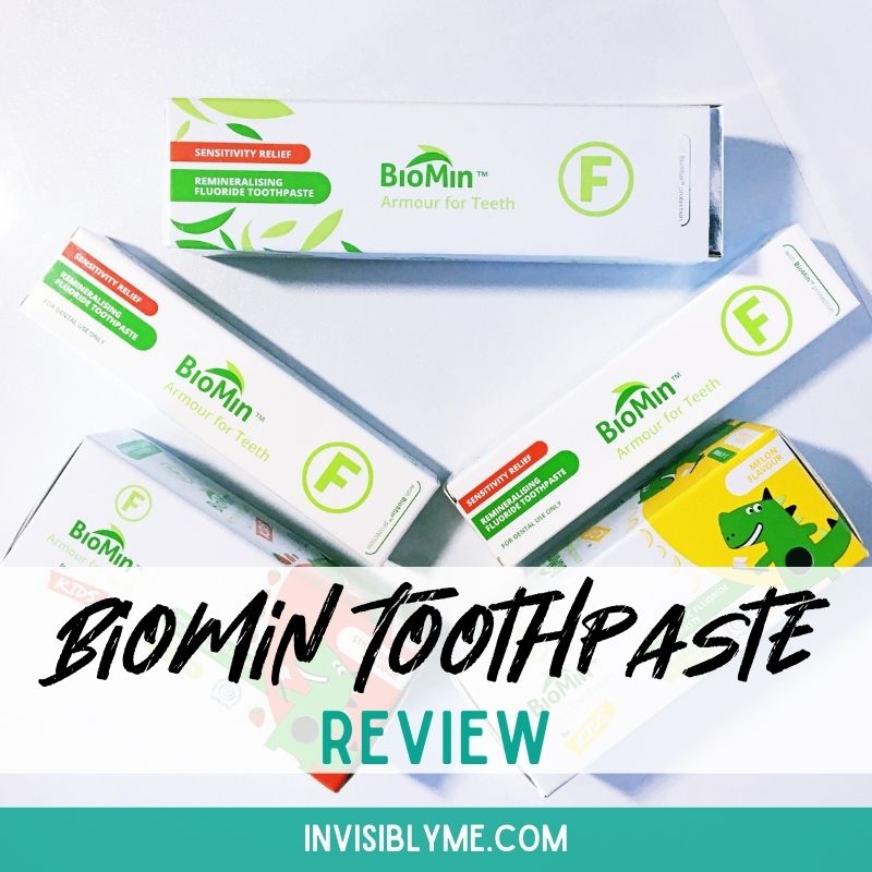 A photo I took of five boxes of BioMin toothpaste from a birds-eye view on my white desk. The boxes are white with red and green detailing. Overlaid is the post title: BioMin Toothpaste Review.