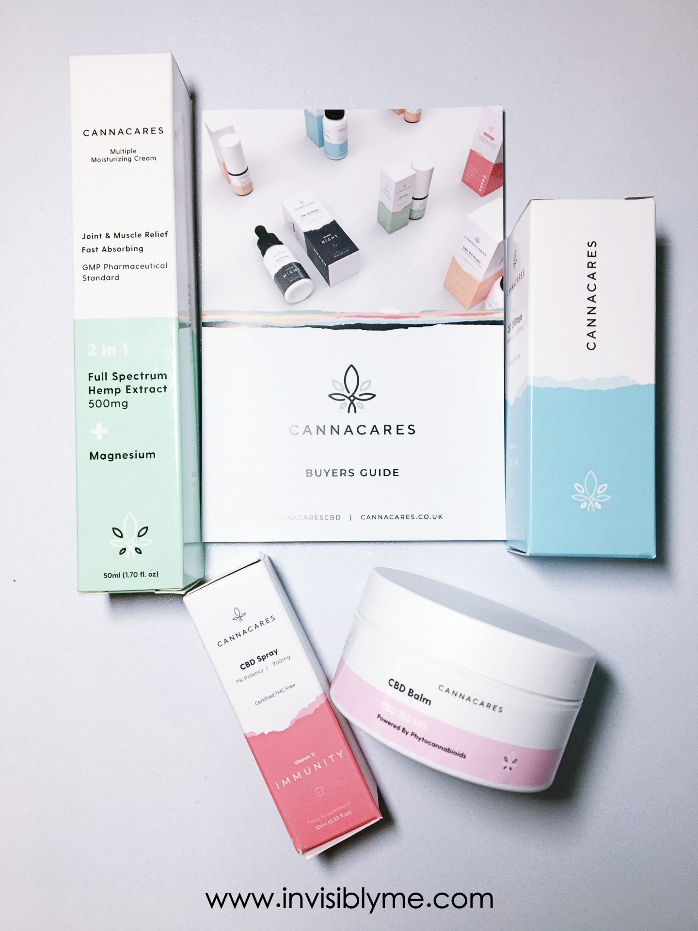 A bird's eye view of the four Cannacares products I was gifted for my review, as well as a brochure. The products are boxed, apart from the balm which comes in a tub. the design is mostly white, very contemporary with pink, blue and green detailing on the different boxes. Below the products is the InvisiblyMe blog branding.