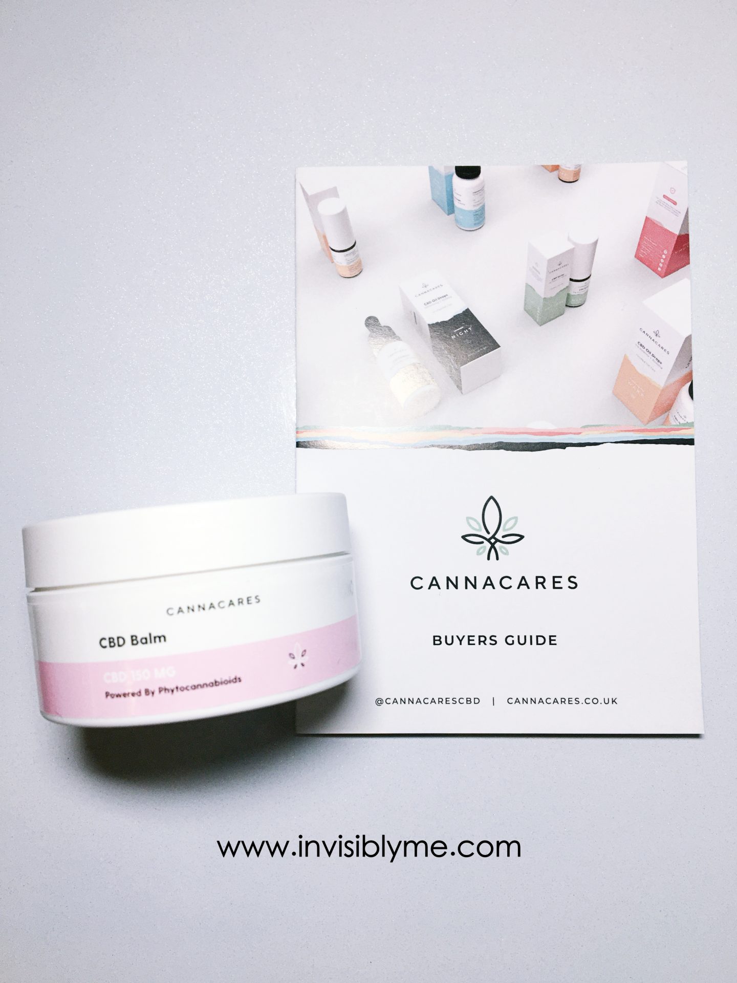 A bird's eye photo of the white and white and pink round tub of CBD balm from Cannacares for my review on top of the brochure.