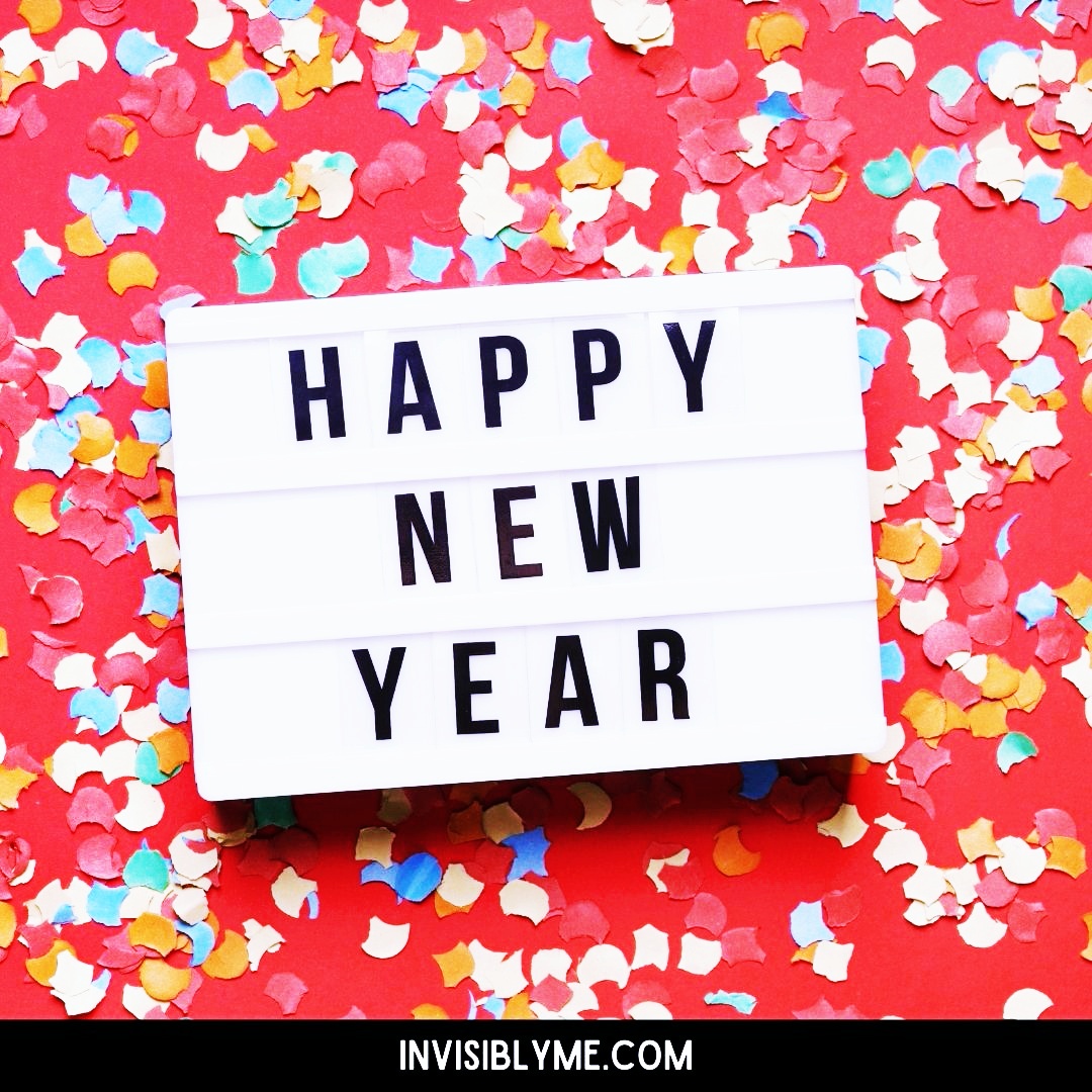 A red background with colourful confetti. In the middle is a light box with the letters spelling out 'Happy New Year'. At the bottom is the Invisibly Me banner.