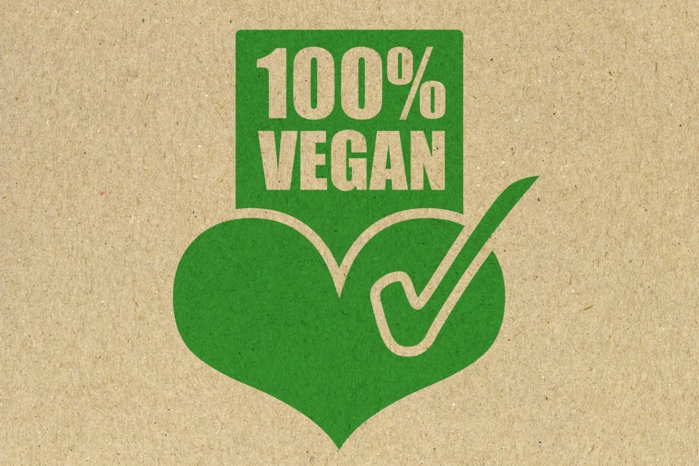A photo of a cardboard background with a fully green icon design showing a heart with a tick through it and '100% vegan' above it.