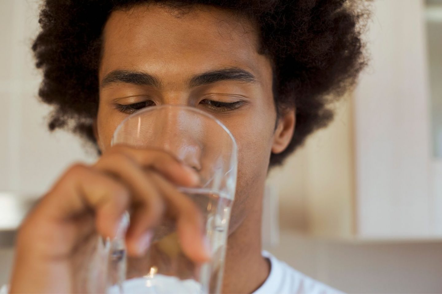 A close-up photo of a man raising a glass of water to his mouth to drink.
