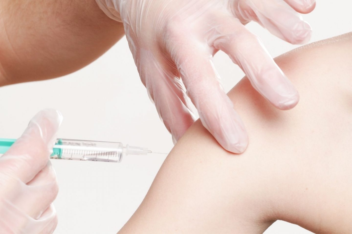 A close up photo of a bare arm at the top by the shoulder and a nurse with clear plastic gloves holding the arm. With her other hand she's injecting the arm.