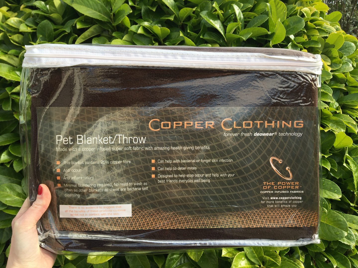A close-up photo of the Copper Clothing pet blanket I was gifted for this review. It's inside the bag it comes in when I received it, which is clear with a white zipper around the top. The blanket itself is brown.