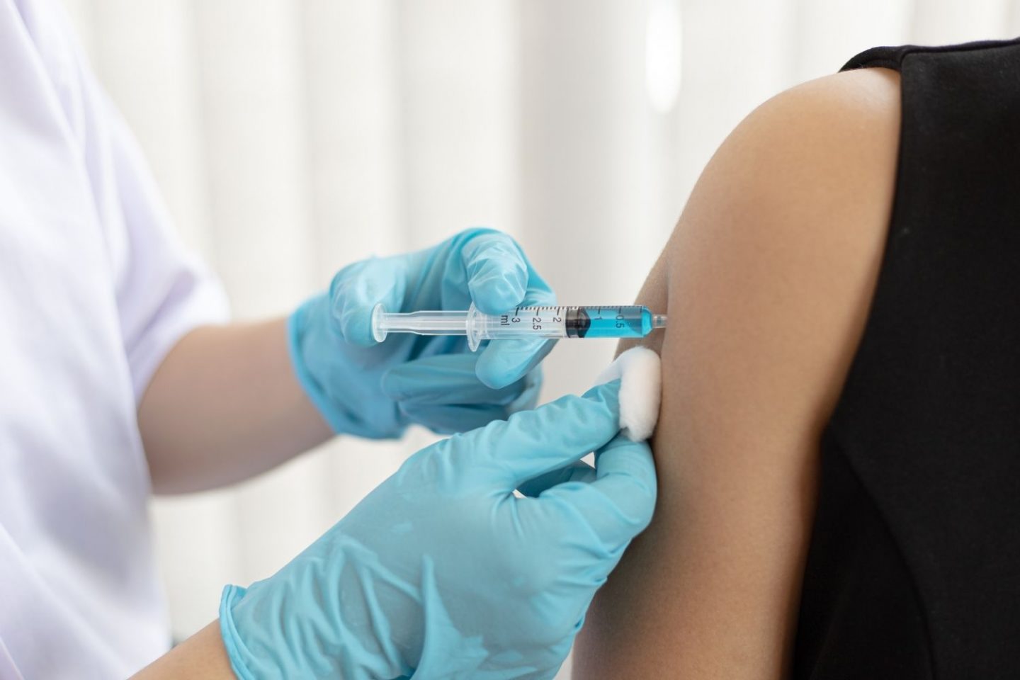 A close-up photo of a bare arm as a doctor injects them with a blue liquid in a syringe.