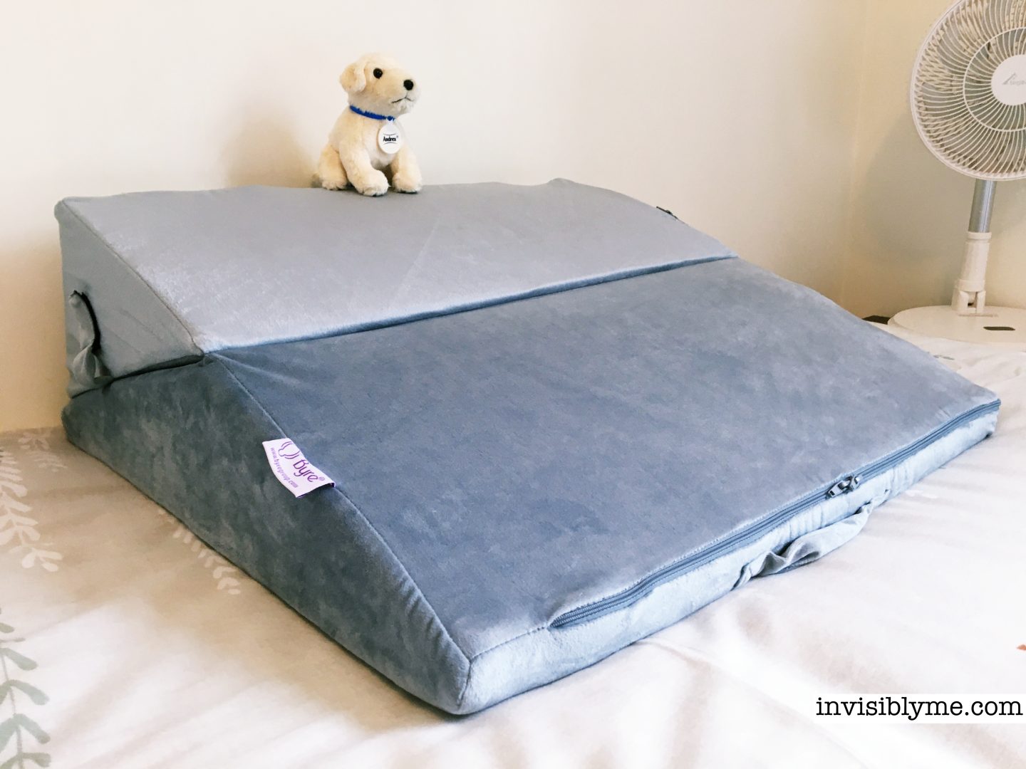 A photo of the Byre folding bed wedge for this review sat on my duvet cover on my bed against a cream wall. It's downwards for a slope to lie on. An Andrex soft puppy toy sits on top.