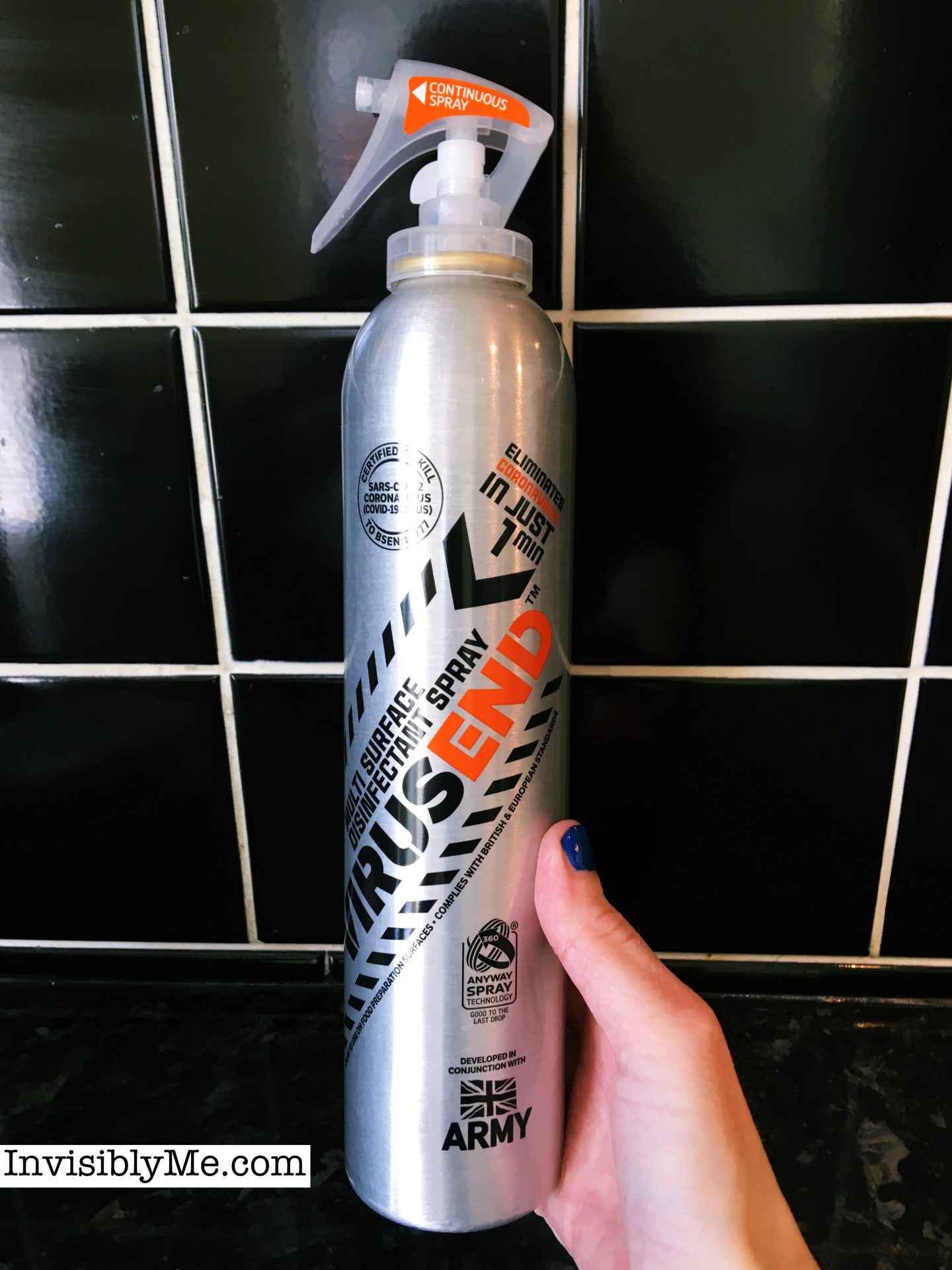 A photo of me holding the silver Virusend canister spray for the Deft and Virusend review against the black tiles in my kitchen.