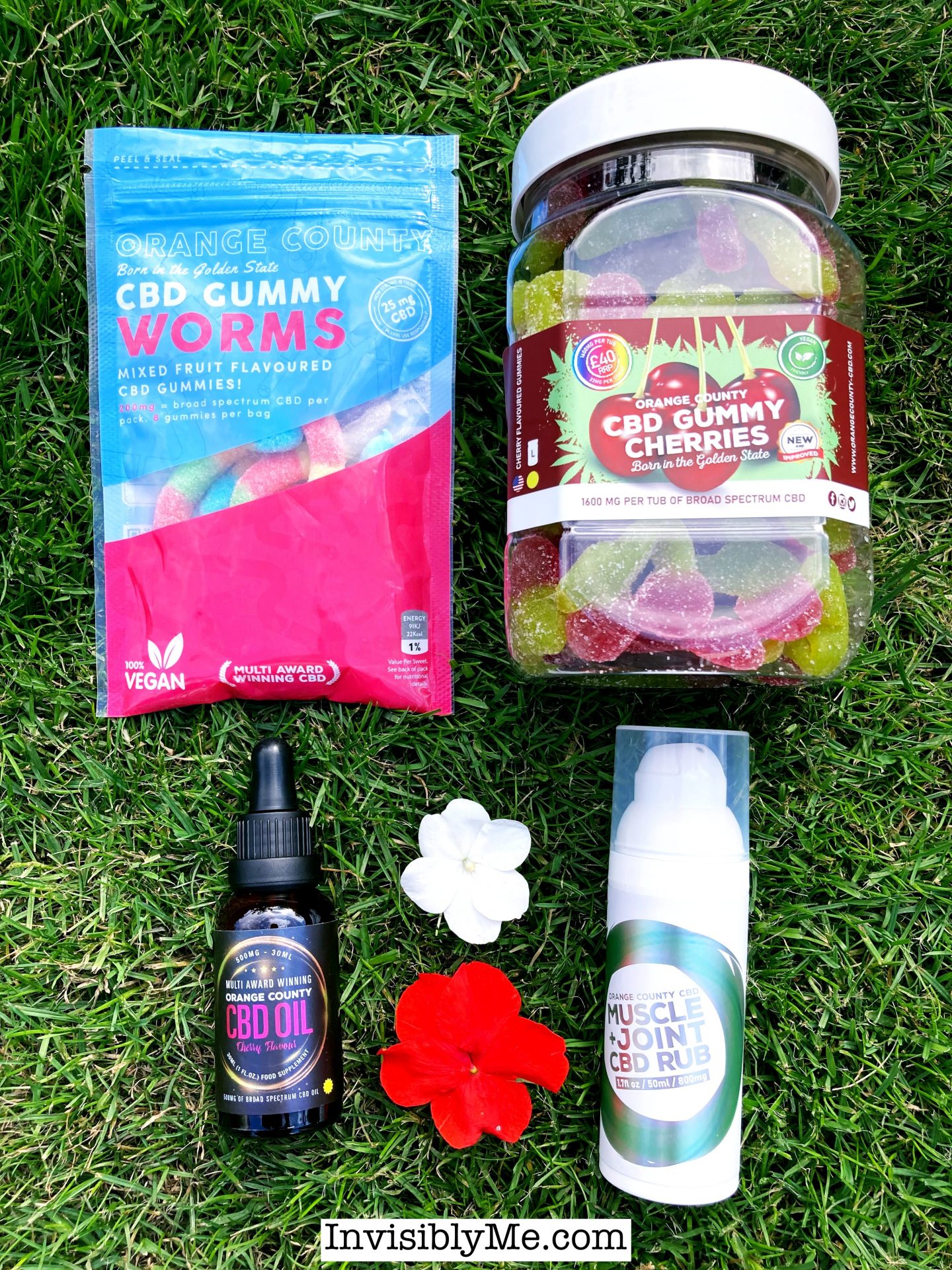 A bird's eye view on the grass of the four products from Orange County for this review. A red flower and a white flower are between the products to add some extra colour.