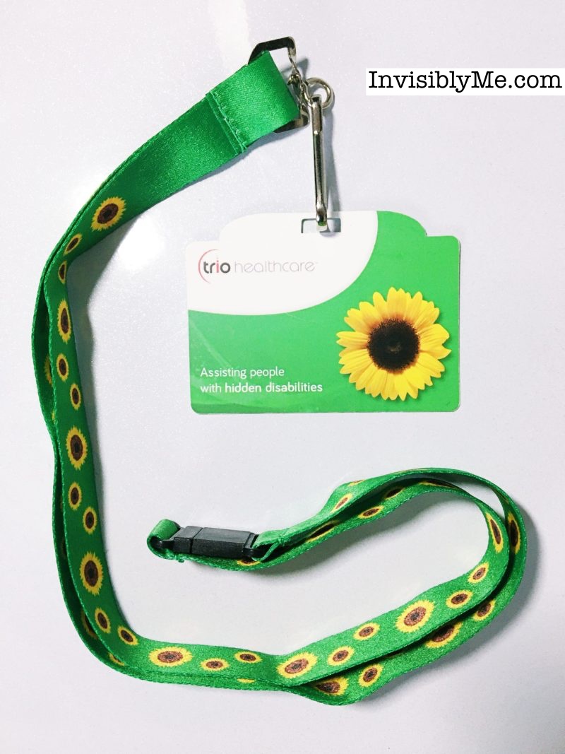The Sunflower Lanyard for Hidden Disabilities. It's a green silky lanyard to go around your neck, with bright yellow sunflower heads all over as the pattern. Mine has a cardboard sign attached to the end from Trio as it was ordered from their website. The InvisiblyMe branding is at the top.