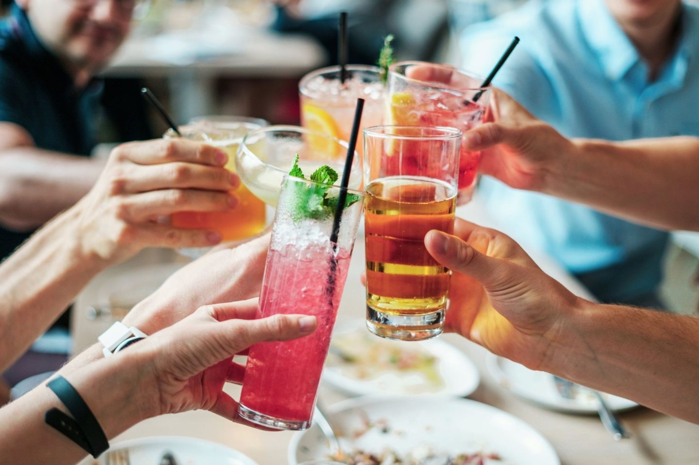 A photo of several hands holding glasses of colourful drinks we assume are alcohol as they clink them together in celebration.