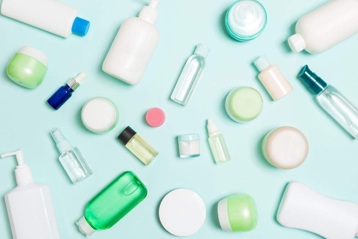 A bird's eye view of numerous bottles, sprays and pots against a light blue background to suggest beauty products and toiletries.
