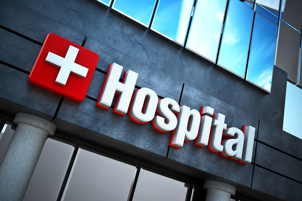 A photo of the front of a hospital close up showing the Hospital sign with white cross.