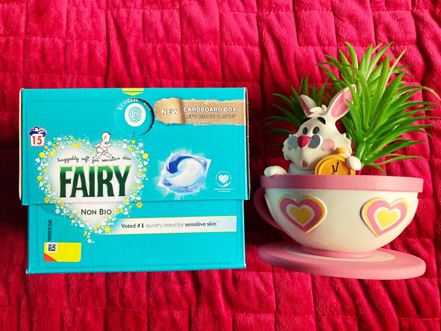 A photo of one of the Fairy Outdoorables products against a red blanket. A teacup and saucer-style potted plant in the style of Alice In Wonderland with the White Rabbit in it sits to the right of the product.