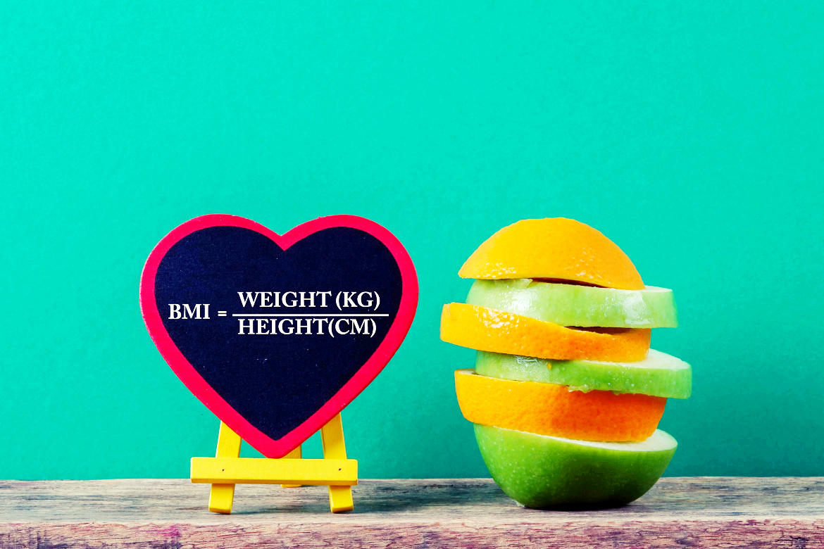 To the right is sliced fruit stacked up, which looks like apples and oranges. To the left of that is a mini heart-shaped chalk board which shows the calculation for BMI as weight divided by height.