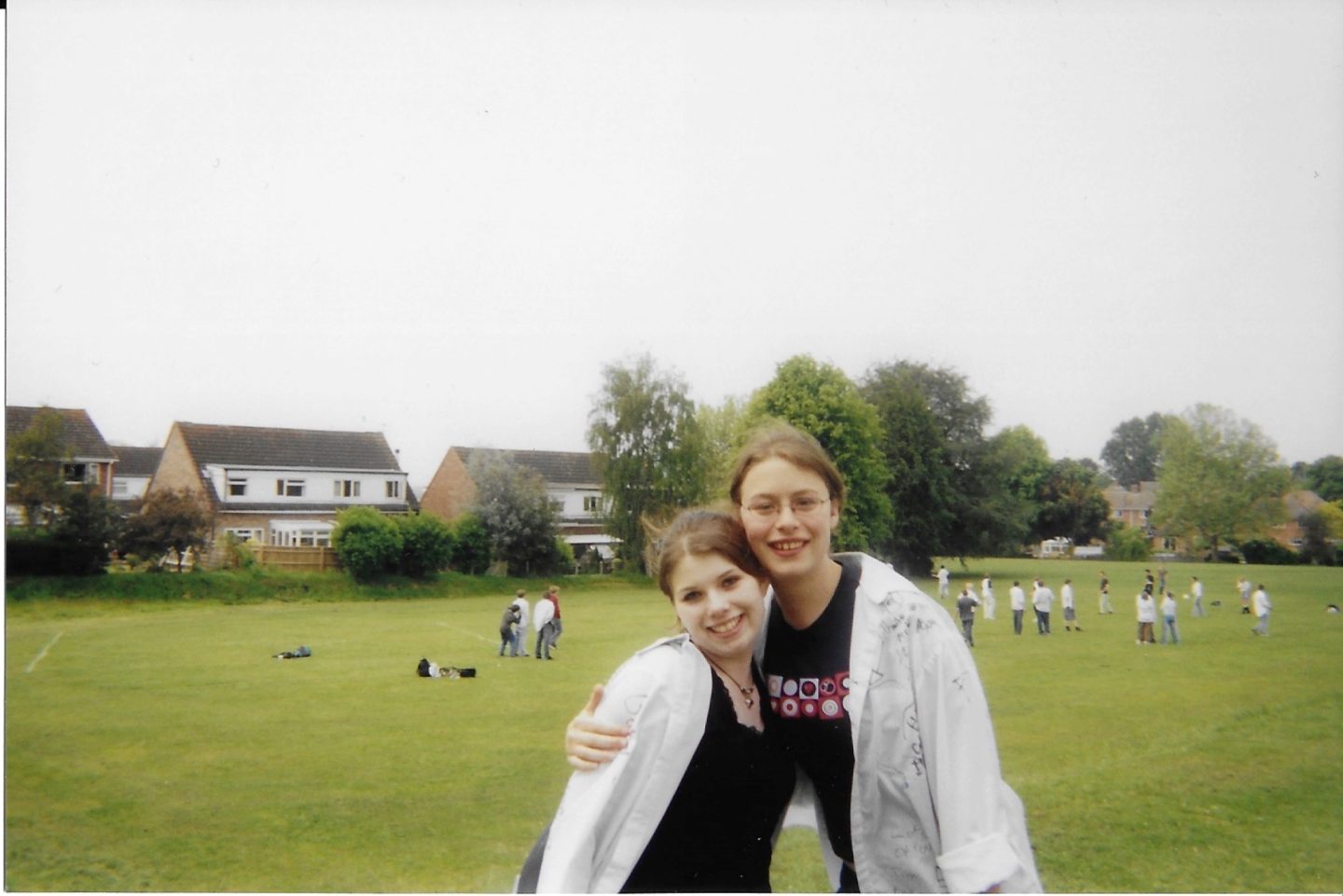 A photo of Caz and Abi hugging on the playing field for the last day of High School, while wearing their signed school shirts.