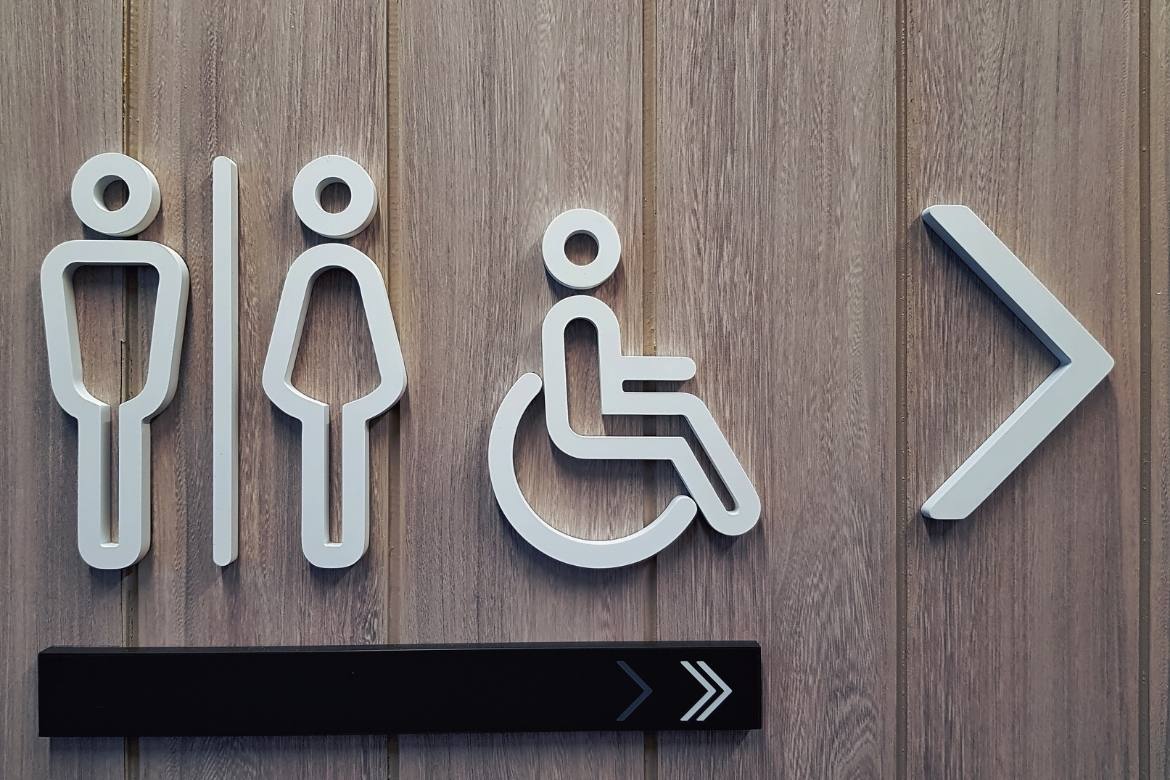 Raised symbols on a door that show an arrow pointing right and a symbol each for men's, women's and disabled toilets.