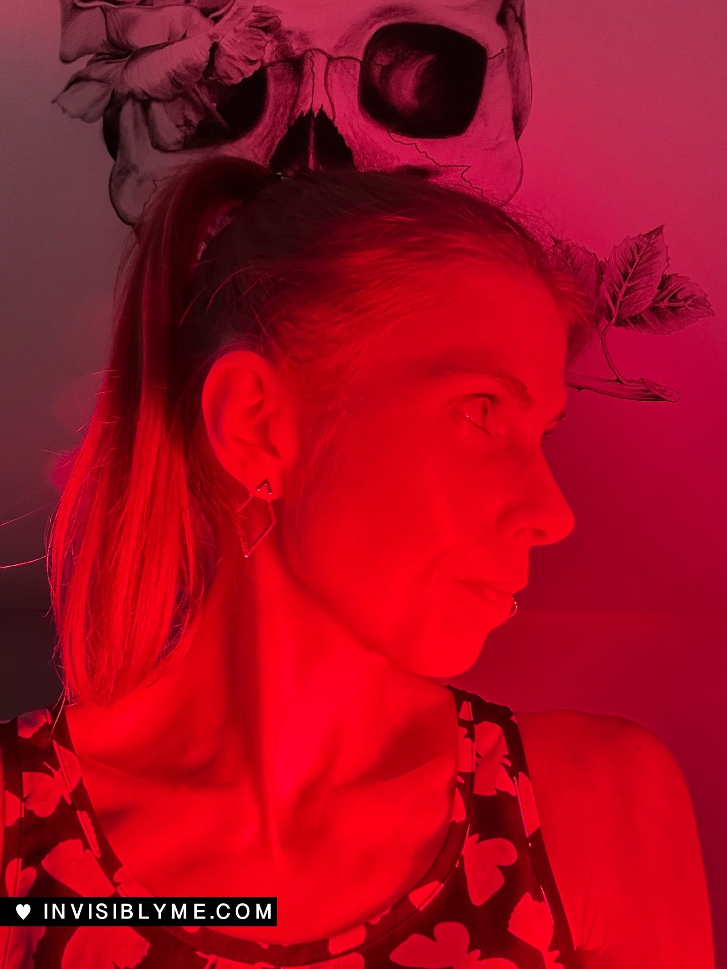 A photo of me turning my head to the side. I'm cast in a red glow as I'm standing in front of the Vital Red Light device.